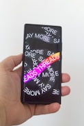 A hand holding a smartphone with a screen displaying overlapping text in white saying 'SAY MORE' multiple times. There is a vibrant gradient text 'THREADS' in the foreground.