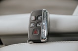 A Range Rover key fob rests on a light-colored leather surface. The fob features various buttons including lock, unlock, headlights, and hazard warning.
