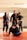 Five people wearing martial arts uniforms are gathered together in a dojo, smiling and interacting with each other. The environment is well-lit, with visible mats on the floor. The mood appears lighthearted and friendly.