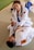 Two people are practicing Brazilian Jiu-Jitsu on a mat, wearing white gis with various patches. One person, smiling with braided hair, is in a top position, appearing to demonstrate a technique on the other person lying on their back.