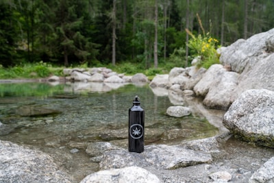 A vibrant outdoor scene showing a hiker holding a Laughing Dead MC Inc water bottle near a mountain stream.