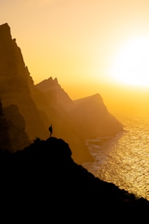 A cinematic shot of a luxury traveler standing on a cliff overlooking a golden sunset over a serene beach.