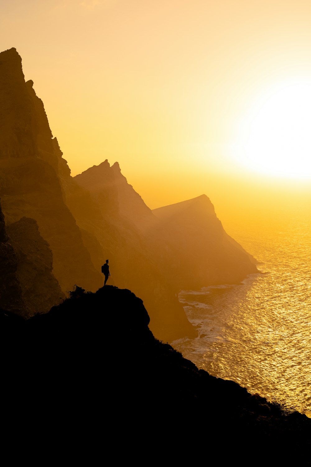 a person standing on top of a mountain next to the ocean