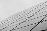 A series of reflective glass panels arranged in a geometric pattern, creating a dynamic diagonal line that extends toward the sky. The panels are secured with bolts, and each panel features intersecting lines forming a grid-like appearance, contributing to a modern architectural aesthetic.