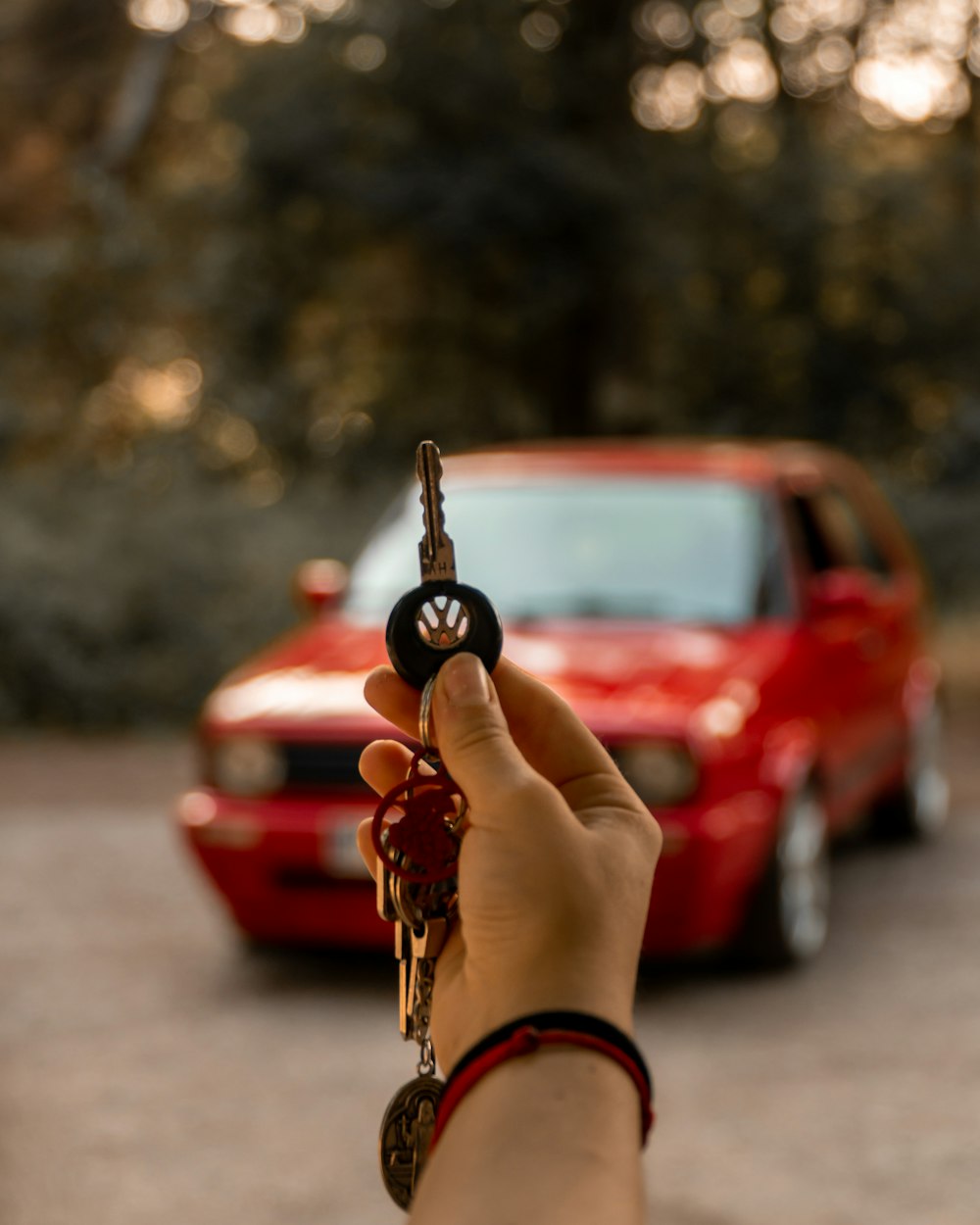 a person holding a car key in front of a red car