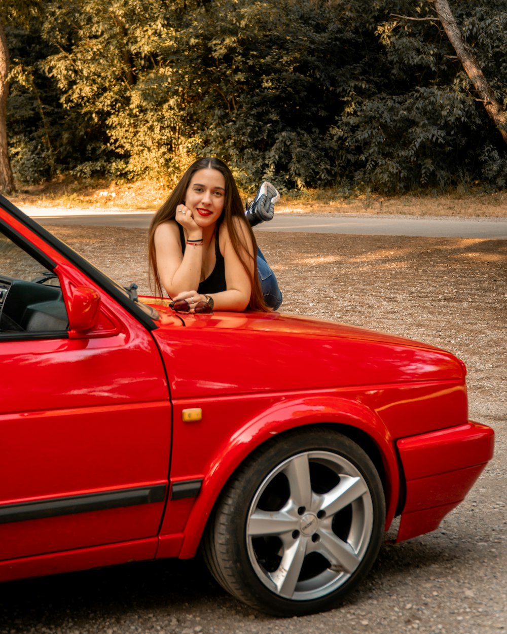 a woman leaning on the hood of a red car