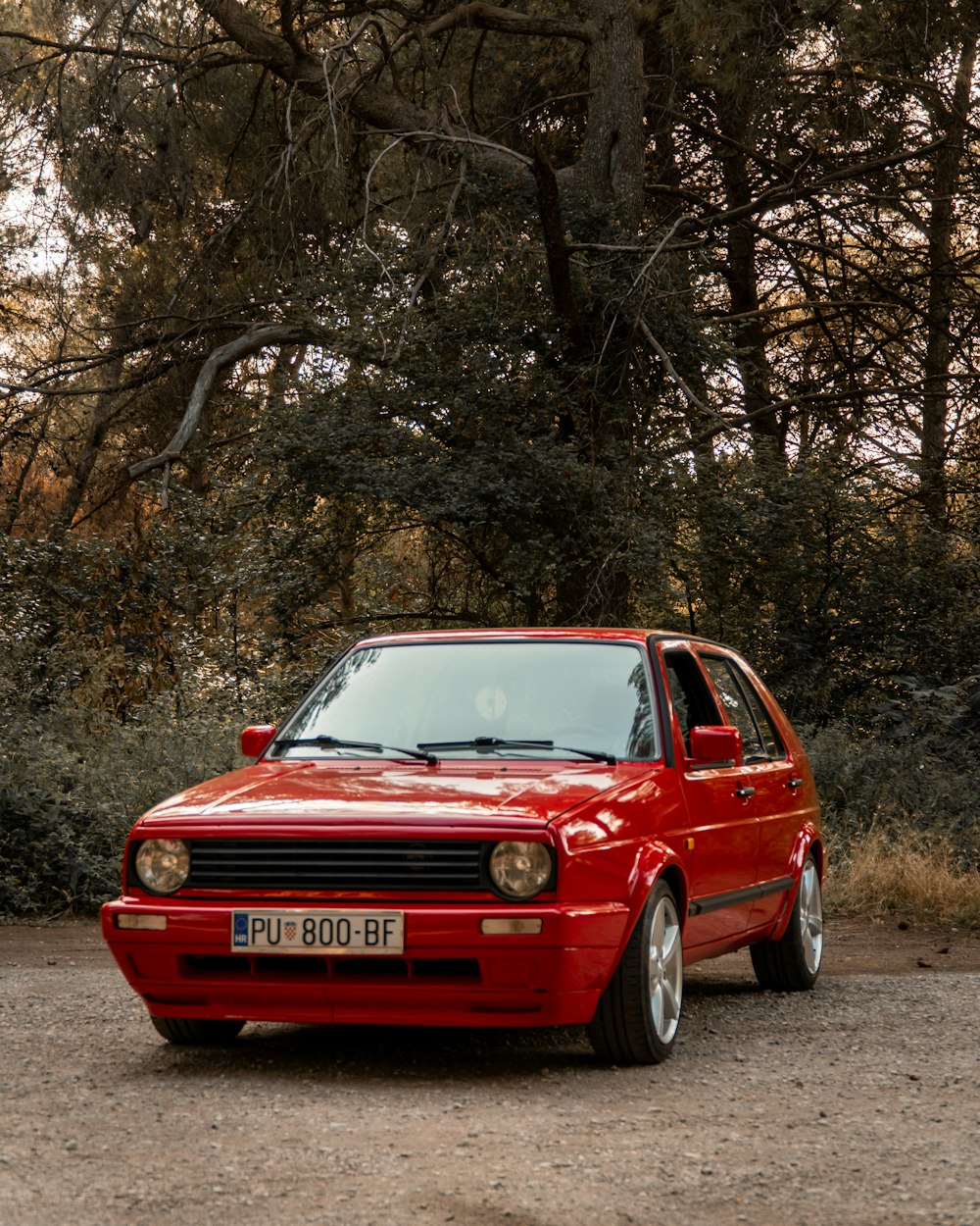 a red car parked in front of some trees