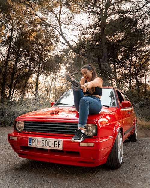 a woman sitting on the hood of a red car