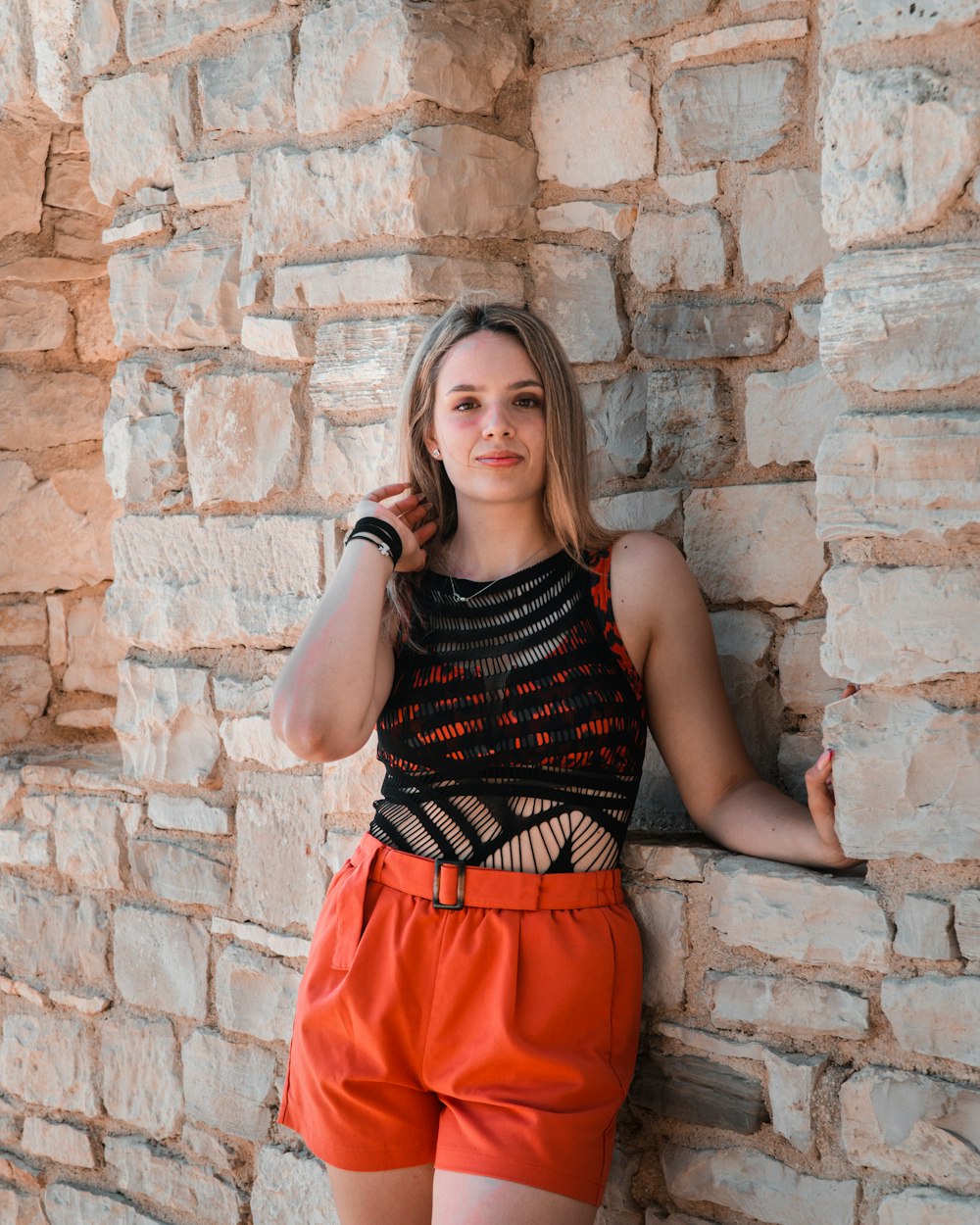 a young woman leaning against a stone wall