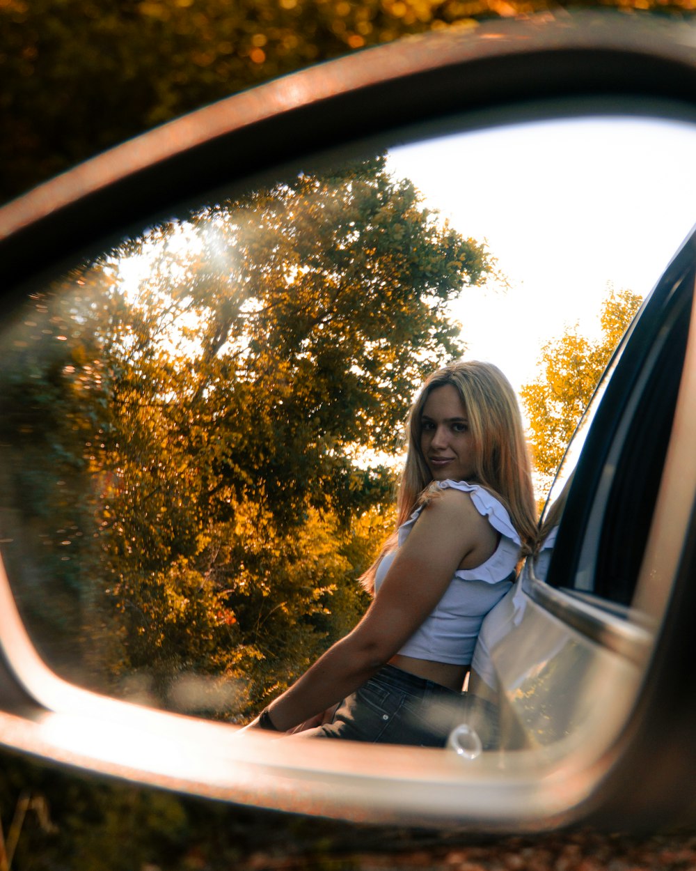 a woman taking a picture of herself in the side view mirror of a car