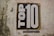 A textured wall features a large poster with the words 'TOP 10' in bold black and white lettering. Below the main text, a smaller phrase reads 'solutions for the common good'.