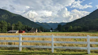 A peaceful rural scene showing a lot with a small wooden fence and distant mountains.