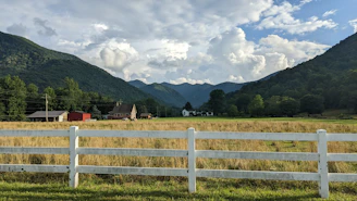 A peaceful rural scene showing a lot with a small wooden fence and distant mountains.