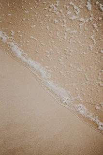 Gentle ocean waves with white foam rolling onto a sandy beach shore.