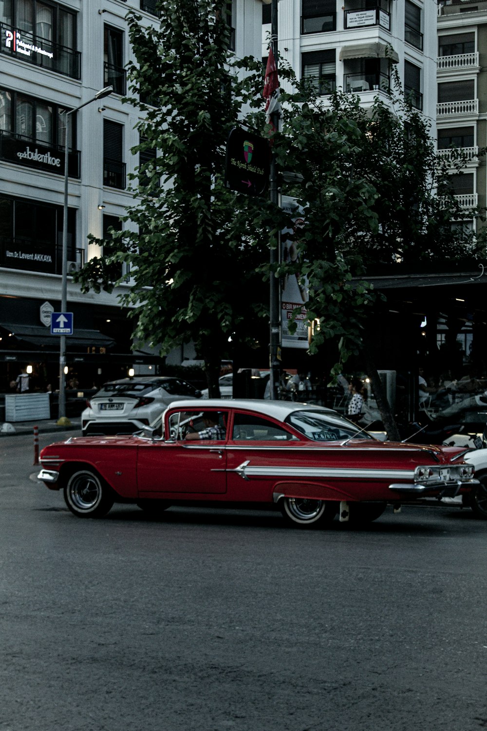 a red car driving down a street next to tall buildings