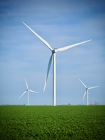 three wind turbines in a green field with a blue sky in the background
