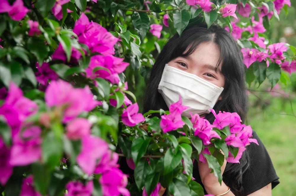 a woman wearing a face mask hiding behind a bush of flowers