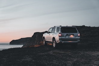 A scenic silver SUV parked by the Brahmaputra River at sunset in Assam.