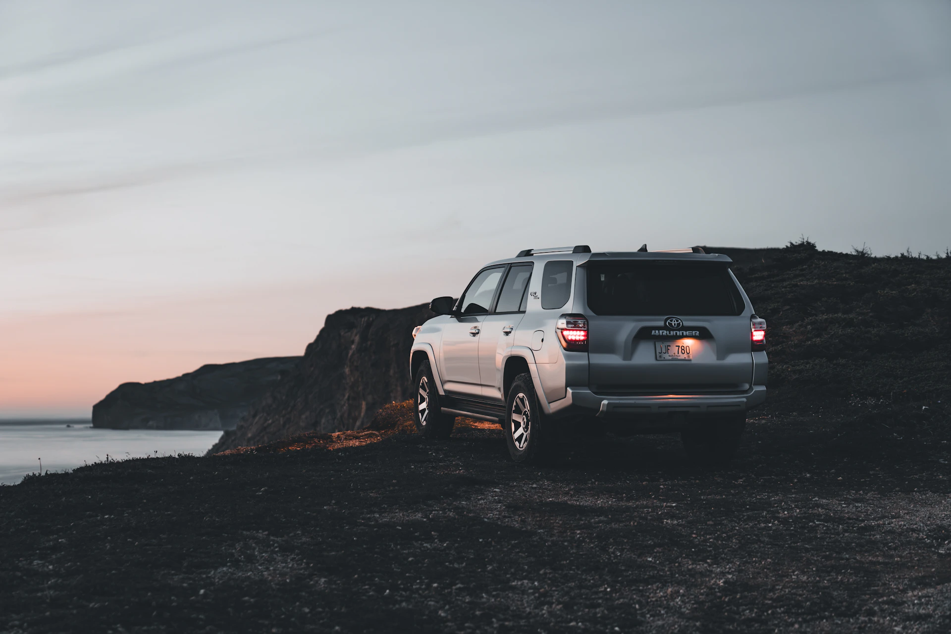 A sleek silver SUV parked by a scenic coastal road at sunset, highlighting adventure and comfort.