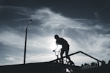 A shadowy figure performing a BMX trick under flickering streetlights with smoky urban backdrop.