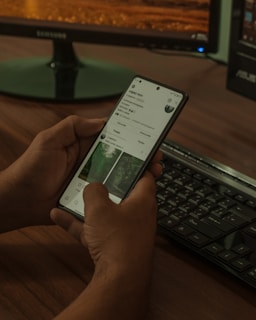 a person holding a cell phone while sitting in front of a computer