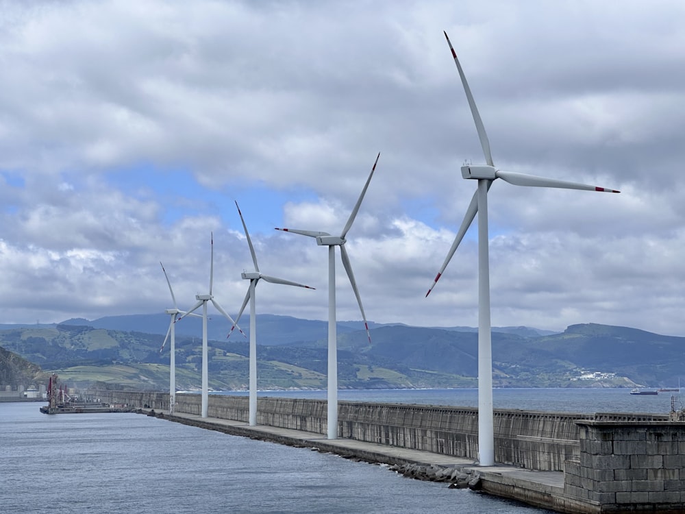 a row of wind turbines next to a body of water