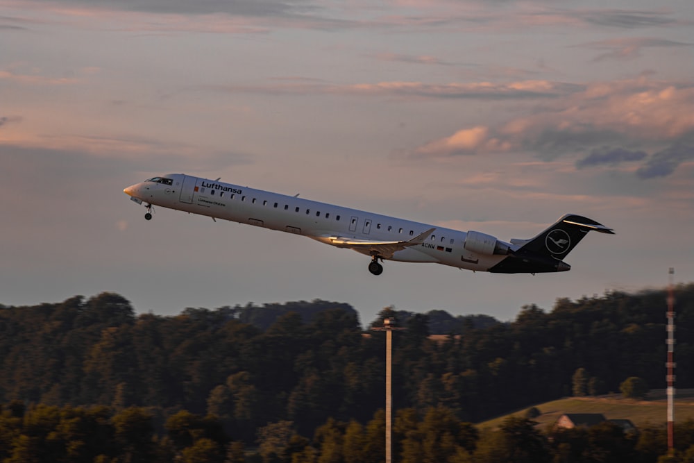 a white and black jet airliner flying over trees