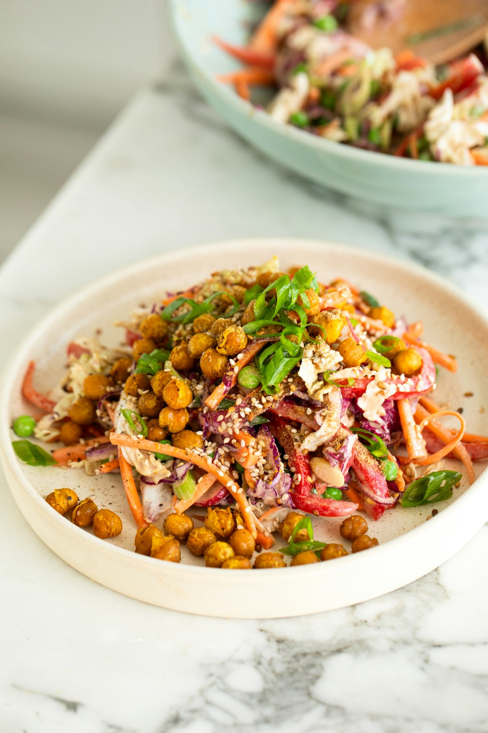 a white plate topped with a salad next to a bowl of salad