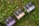 Several boxes with elegant designs labeled with different product names are placed on a patch of green grass and clover. The boxes have distinct typography and color schemes, including shades of purple, blue, and beige.