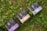 Several boxes with elegant designs labeled with different product names are placed on a patch of green grass and clover. The boxes have distinct typography and color schemes, including shades of purple, blue, and beige.