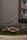 A brown sofa set, including a couch and an armchair, is placed on a patch of grass next to a sidewalk. The setting is in front of a gray concrete building with apartment balconies. A 'No Dumping Allowed' sign is visible on the wall behind the furniture.