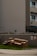 A brown sofa set, including a couch and an armchair, is placed on a patch of grass next to a sidewalk. The setting is in front of a gray concrete building with apartment balconies. A 'No Dumping Allowed' sign is visible on the wall behind the furniture.