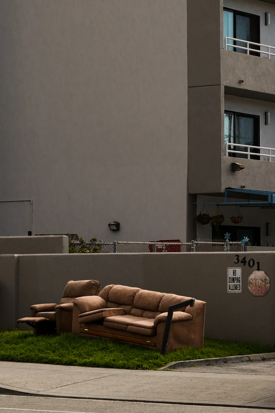 Old couch and recliner left on a curbside patch of grass beside an apartment building