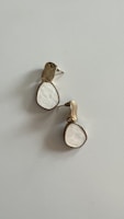 A pair of earrings with a modern design, showcasing a teardrop shape. They feature a combination of metallic and white-colored elements, with a unique texture.