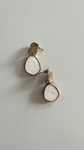 A pair of earrings with a modern design, showcasing a teardrop shape. They feature a combination of metallic and white-colored elements, with a unique texture.