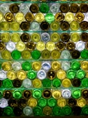 A pattern created by the bottoms of various colored glass bottles arranged in rows. The bottles are primarily green, amber, and clear, reflecting light in a visually striking way.