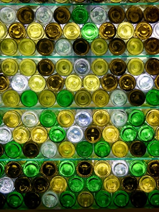 A pattern created by the bottoms of various colored glass bottles arranged in rows. The bottles are primarily green, amber, and clear, reflecting light in a visually striking way.