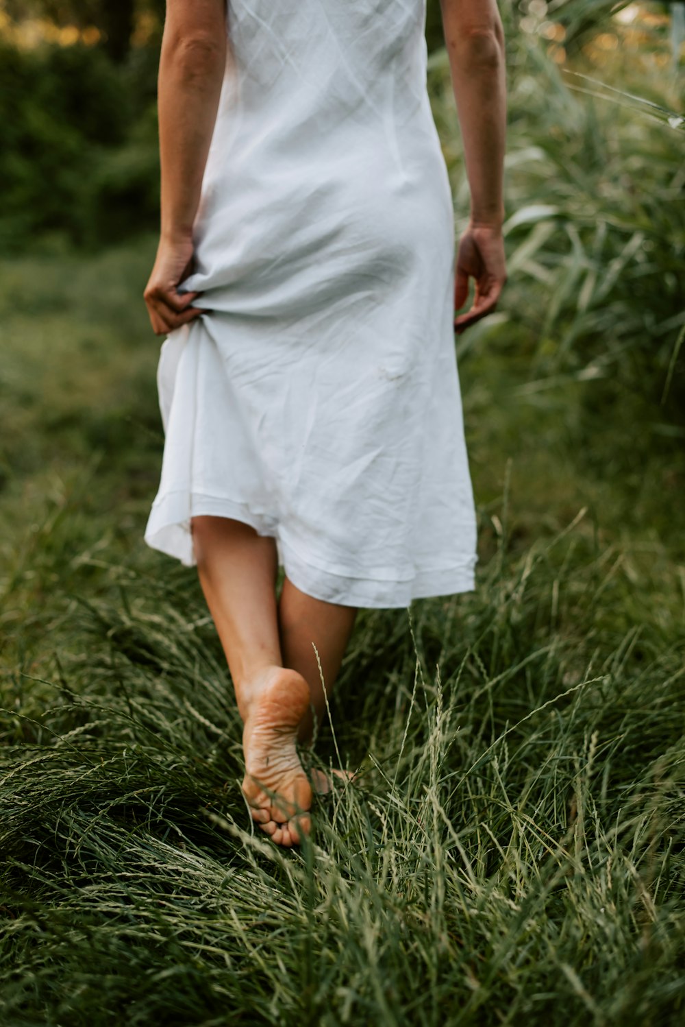 a woman in a white dress walking through tall grass