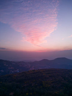 A panoramic view from a summit overlooking rolling hills bathed in soft twilight.