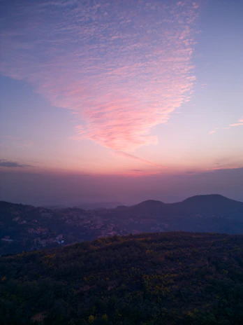A panoramic view from a summit overlooking rolling hills bathed in soft twilight.