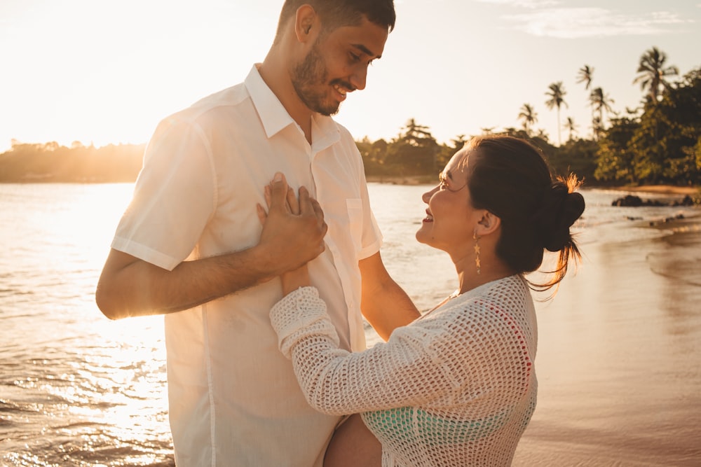 a man and woman standing on a beach next to the ocean