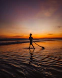 Silhouette of a person walking barefoot along the shoreline at dusk