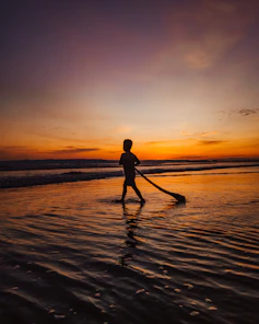 Silhouette of a person walking barefoot along the shoreline at dusk