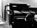 A monochrome image of a black multifunction printer with the brand name visible on the top. The printer displays a control panel and an open paper tray. It is positioned against a plain wall with a small portion of a person or object partially visible in the foreground.