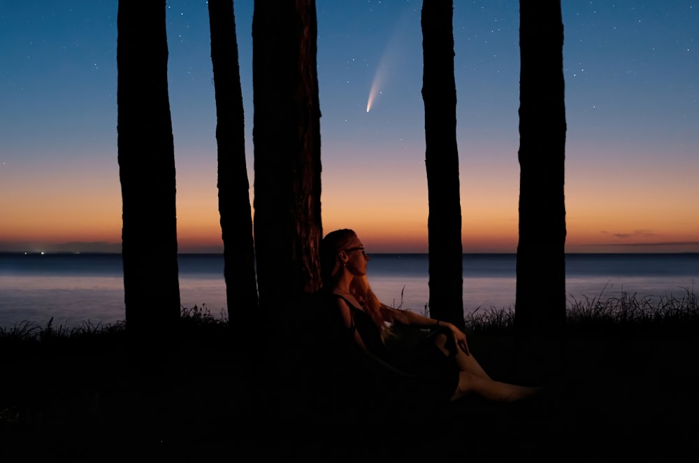 a woman sitting in the shade of some trees