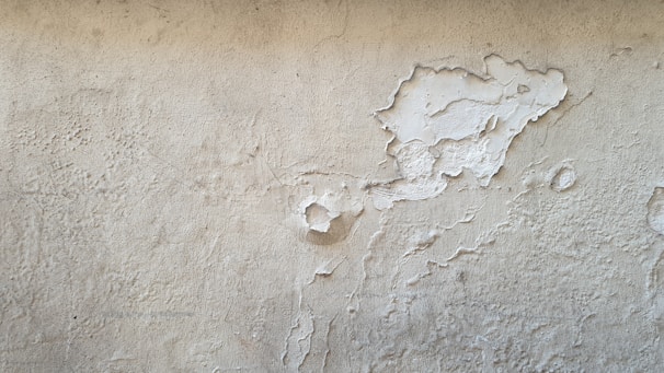 A worn-out living room wall with peeling paint and minor drywall damage.