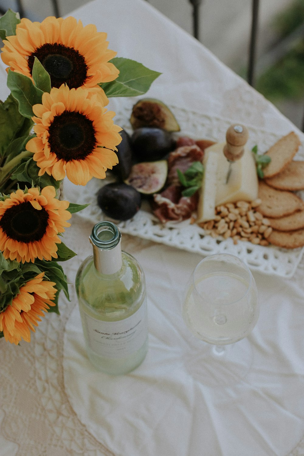 a table topped with a vase of sunflowers next to a bottle of wine