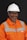 A person wearing an orange safety work uniform with reflective stripes and a white hard hat. The individual is also wearing safety glasses and appears to be smiling.