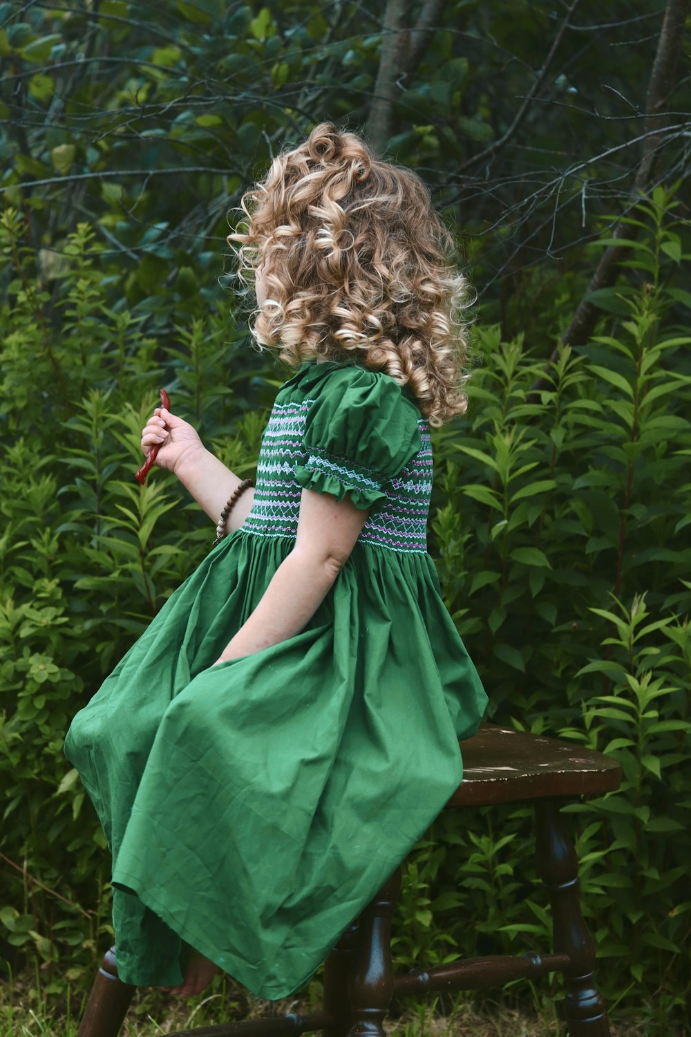 a little girl in a green dress sitting on a bench