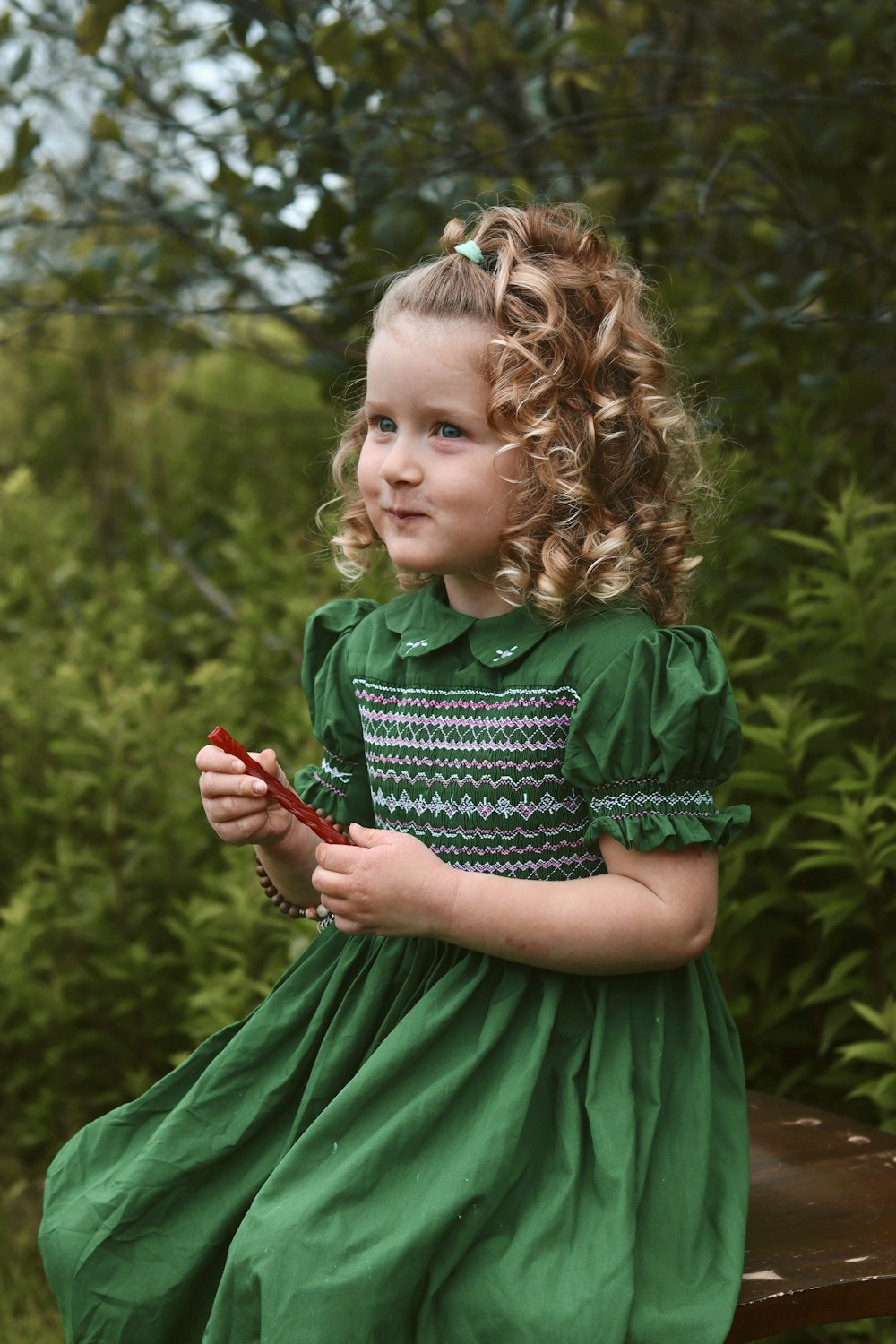 a little girl in a green dress sitting on a bench